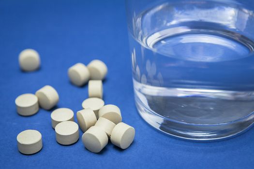Glass of water and pills isolated on blue