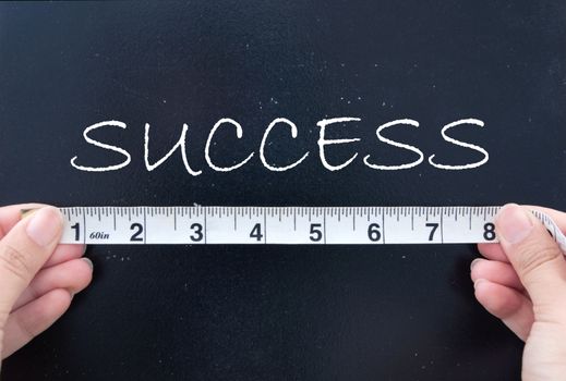 Tape measuring the word success on a chalk board 