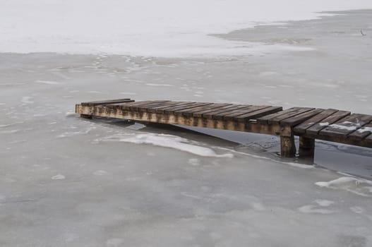 Wooden footbridge on a frozen pond, early spring