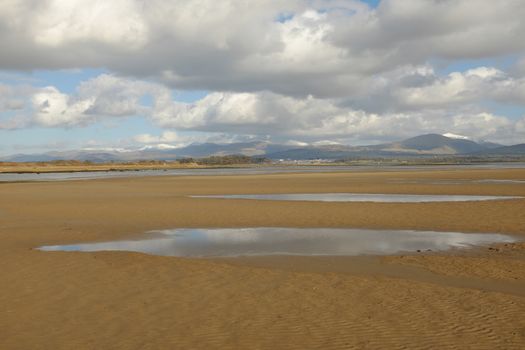 Clean sand on the Menai Straits, Anglesey, UK. with pools of water stretching to the mountains of Snowdonia, Wales, UK, in the distance.