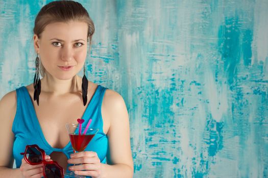 Happy beautiful woman holding a tropical cocktail with sunglasses on bright background