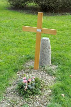 Simple wood cross and flower on a cemetery tomb in green grass