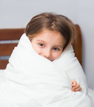 Little girl sitting on the bed wrapped in a blanket
