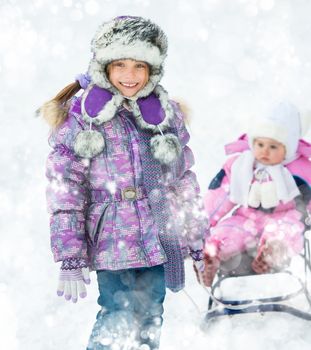 Smiling girl rolls brother on sledge on snow background