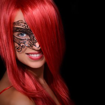 Beautiful red haired woman in carnival mask over black background