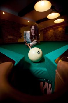 Brunette woman aiming with cue at billiard ball