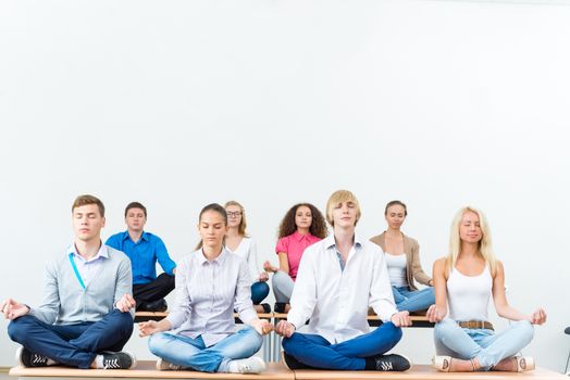 group of young people meditating in office at desk, group meditation