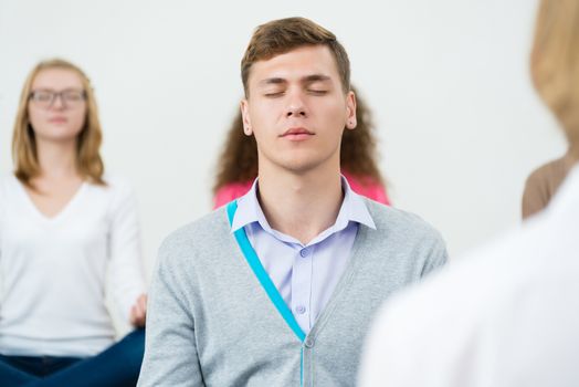 young man, meditating with closed eyes, group meditation