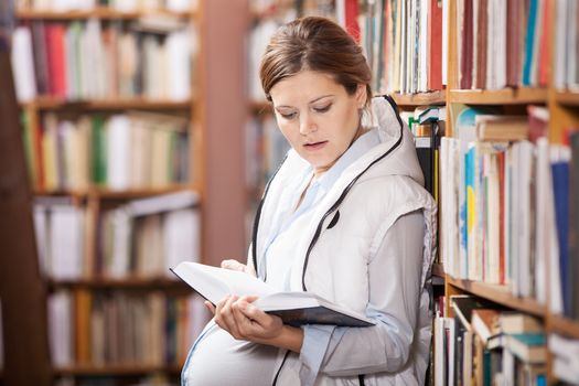 Young pregnant caucasian woman reading book in library