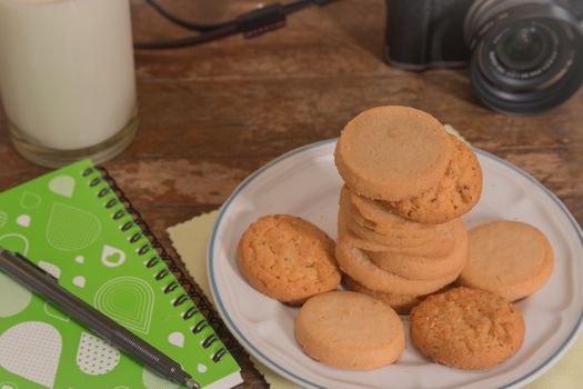 cookies multiple flavors, notebook, camera, milk on wooden table