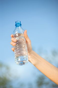 hand holding plastic bottle of water in front of sky