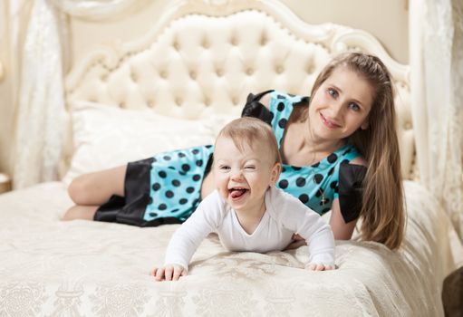 Young Caucasian mother and baby son having fun on bed at home