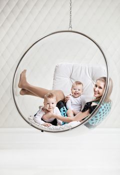 Young Caucasian woman with two babies having fun while sitting in swinging hanging chair