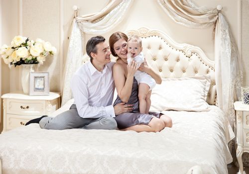 Young happy family with a baby on bed at home