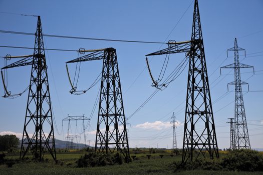pillars with electricity transmitting lines in field under blue skies