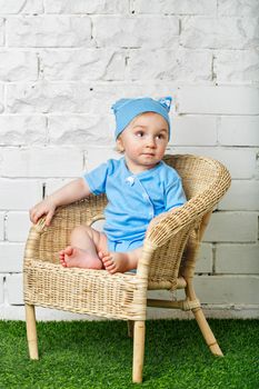 Little boy sitting in a wicker chair on the lawn barefoot