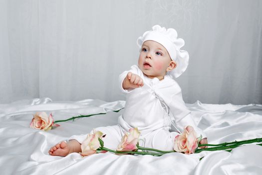 Little girl sitting on silk sheets lie at the feet of flowers