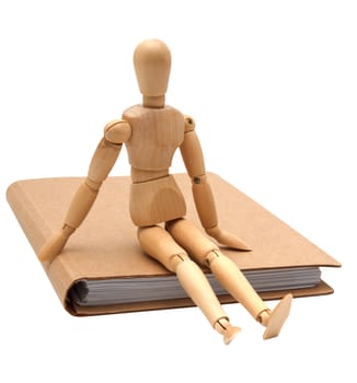 wooden man sitting on brown notebook