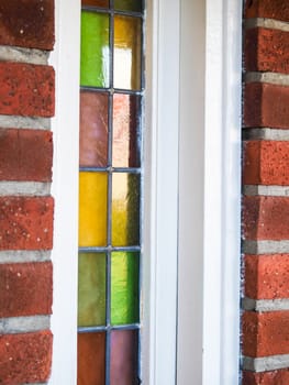 Closeup of small colored glass windows with white frame in a red brick building