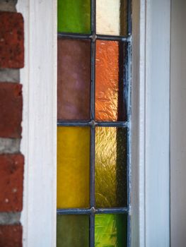 Closeup of small colored glass windows with white frame in a red brick building