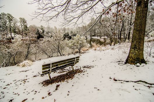 park bench in the snow covered park overlooking lake