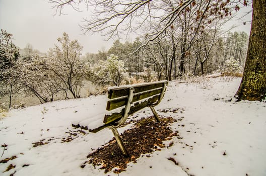 park bench in the snow covered park overlooking lake