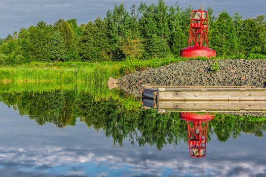 An abandoned red buoy on dry land by a lake and a dock in Ontario, Canada.