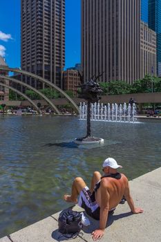 A shirtless man sitting near a fontain in a sunny day, Toronto city, Canada.