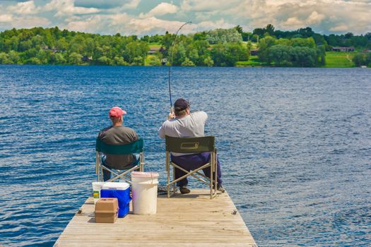 Two fishernem sitting and fishing in a lake.