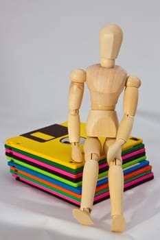 Artist's wooden manikin sitting on diskettes isolated