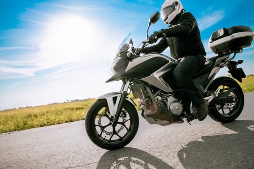 Biker in helmet riding a road motorbike on a sunny day.