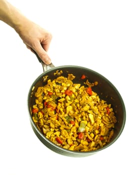 Fry pan with chicken with curry, red pepper and corn held by a male chef towards white background