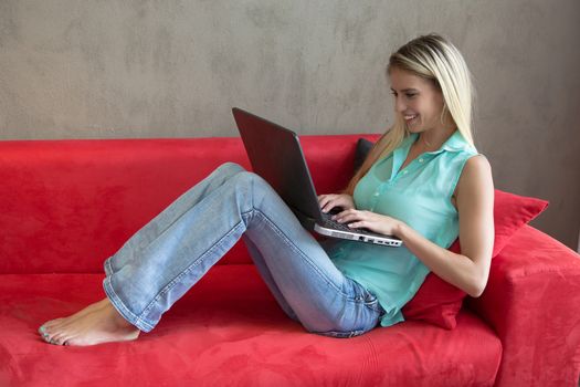 Beautiful blond lady relaxing on a red sofa with her computer