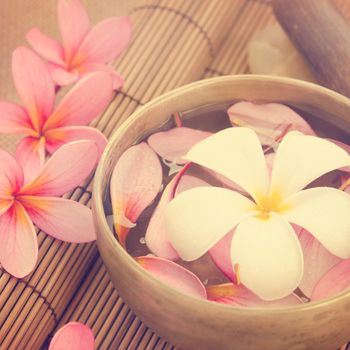 Spa setting, low light with ambient in vintage revival tone. Frangipani, hot and cold stone on bamboo mat.