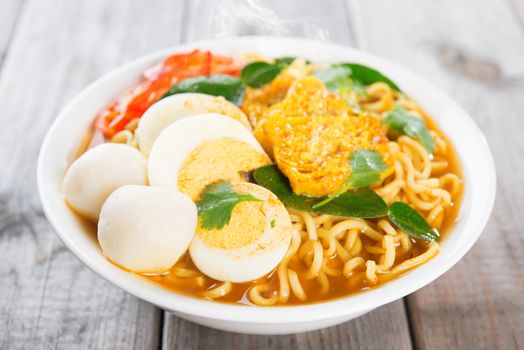 Spicy curry instant noodles soup on wooden dining table. Fresh cooked, hot with steamed smoke.