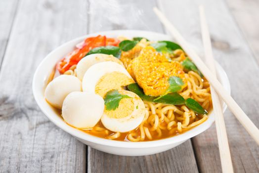 Spicy curry instant noodles soup with chopsticks on wooden dining table. Fresh hot with steamed smoke.