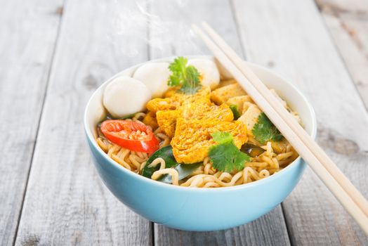 Spicy curry instant noodles soup with chopsticks on wooden dining table. Fresh cooked, hot with steamed smoke.