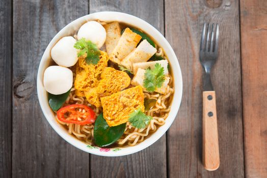 Spicy curry instant noodles soup with fork on wooden dining table. Fresh hot with steamed smoke.