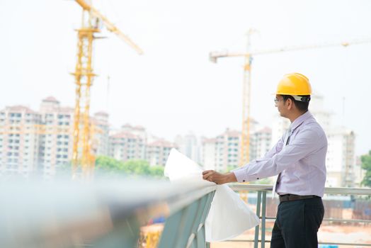 Portrait of a smiling Asian Indian male contractor engineer with hard hat inspecting at construction site.