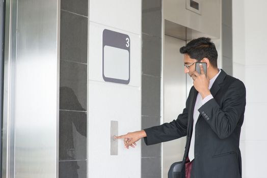 Asian Indian businessman pressing on elevator button, waiting door open to enter inside the lift.