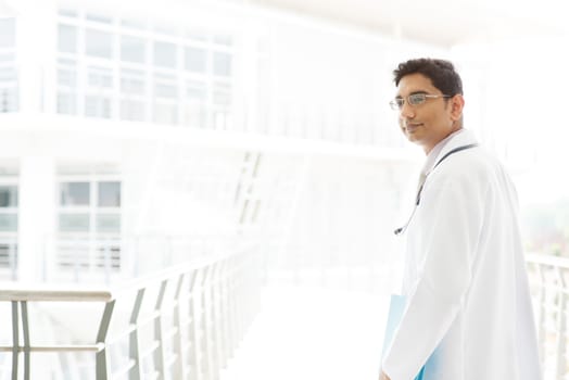 Portrait of a smiling Asian Indian male medical doctor walking inside hospital.