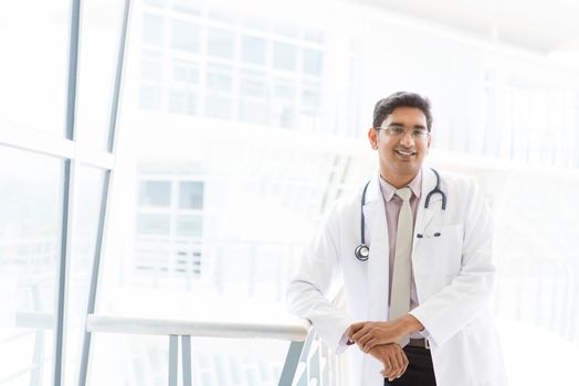 Portrait of a smiling Asian Indian male medical doctor standing inside hospital.