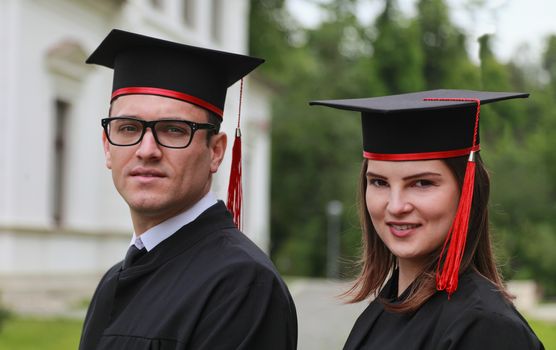 Outdoor portrait of a young couple of students in the graduation day near the university building.