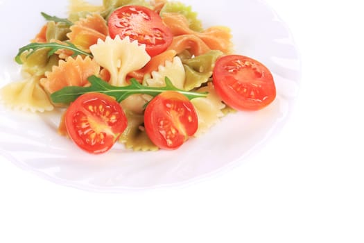 Colored farfalle on white plate with tomatoes. Whole background.