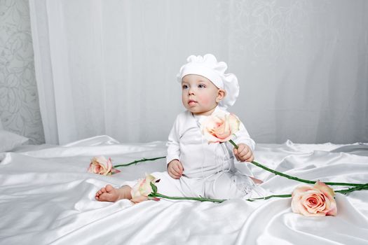 Little girl sitting on silk sheets lie at the feet of flowers