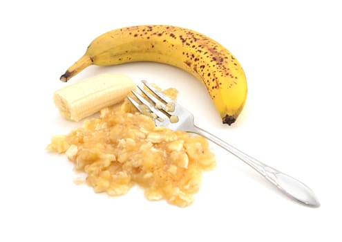 Overripe banana with a fork and pureed fruit, isolated on a white background