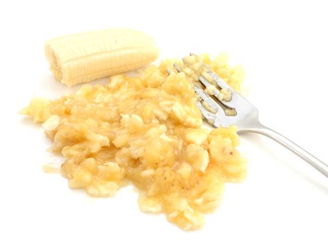 Closeup of mashed and whole banana with a fork, isolated on a white background