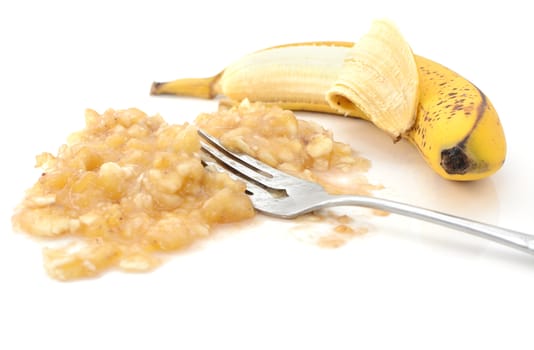 Closeup of half-peeled banana with a fork in mashed puree, isolated on a white background 