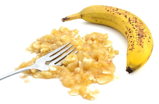 Closeup of mashed banana with fork and an unpeeled fruit, isolated on a white background