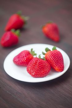 red juicy strawberry in a plate on a wooden surface